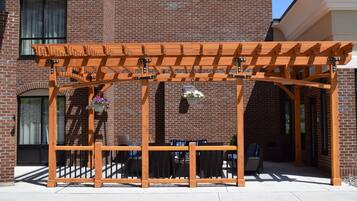 A wooden pergola structure with a brick building in the background.