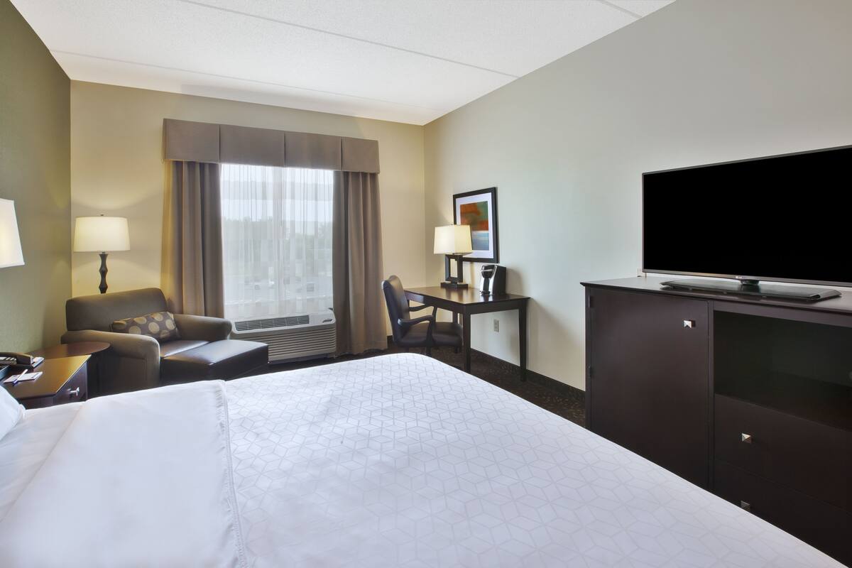 A hotel room with a large bed, a desk, a chair, a television, and a window with curtains.