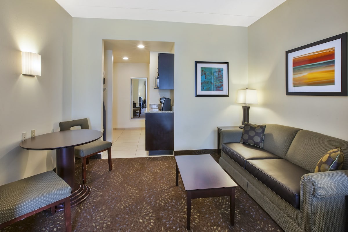 A hotel room with a dining table, a sofa, a coffee table, and a kitchen area in the background.