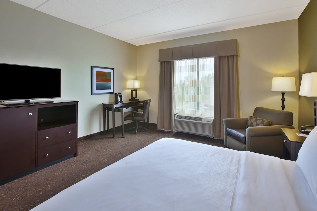 A hotel room with a bed, a desk, a chair, a TV, and a window with curtains.