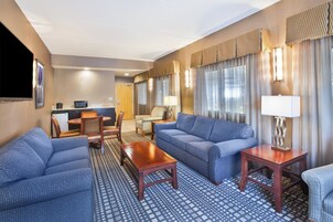 Habitación de hotel con zona de estar, televisor, escritorio y puerta que da a un baño.