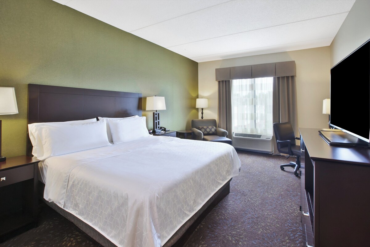 A hotel room with a large bed, a desk, a chair, a television, and a window with curtains.