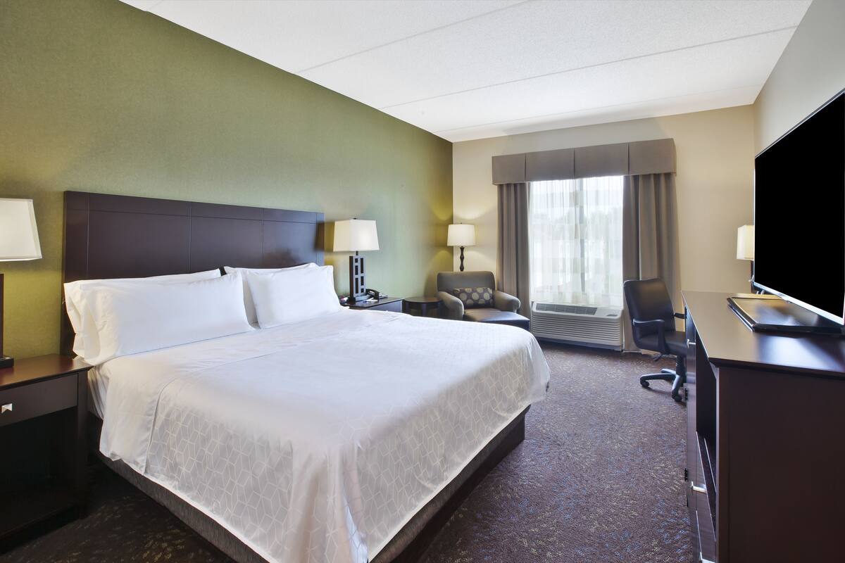 A hotel room with a large bed, two bedside tables with lamps, a desk with a computer, a chair, and a TV.