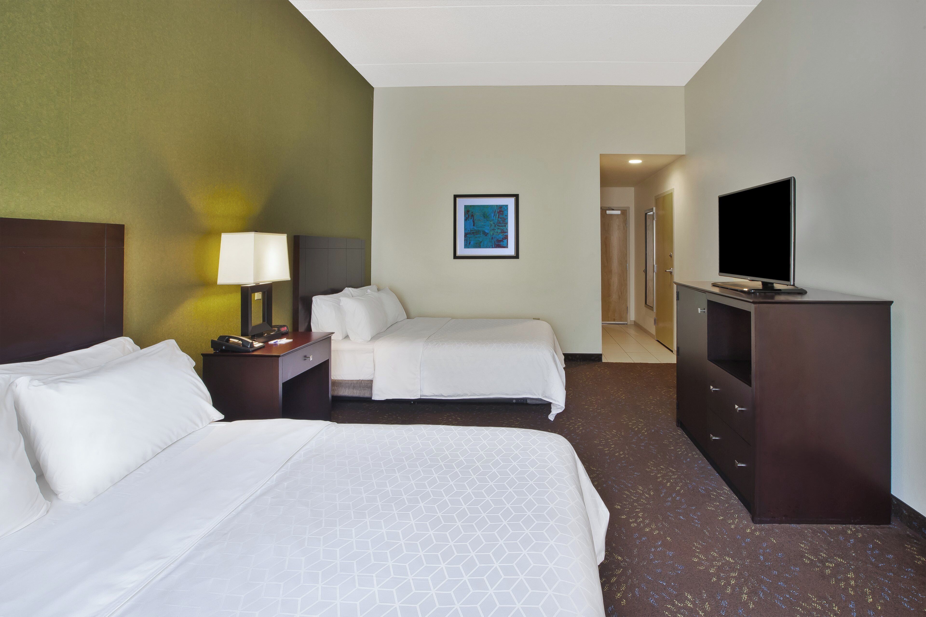 A hotel room with two beds, a desk, a television, and a painting on the wall.