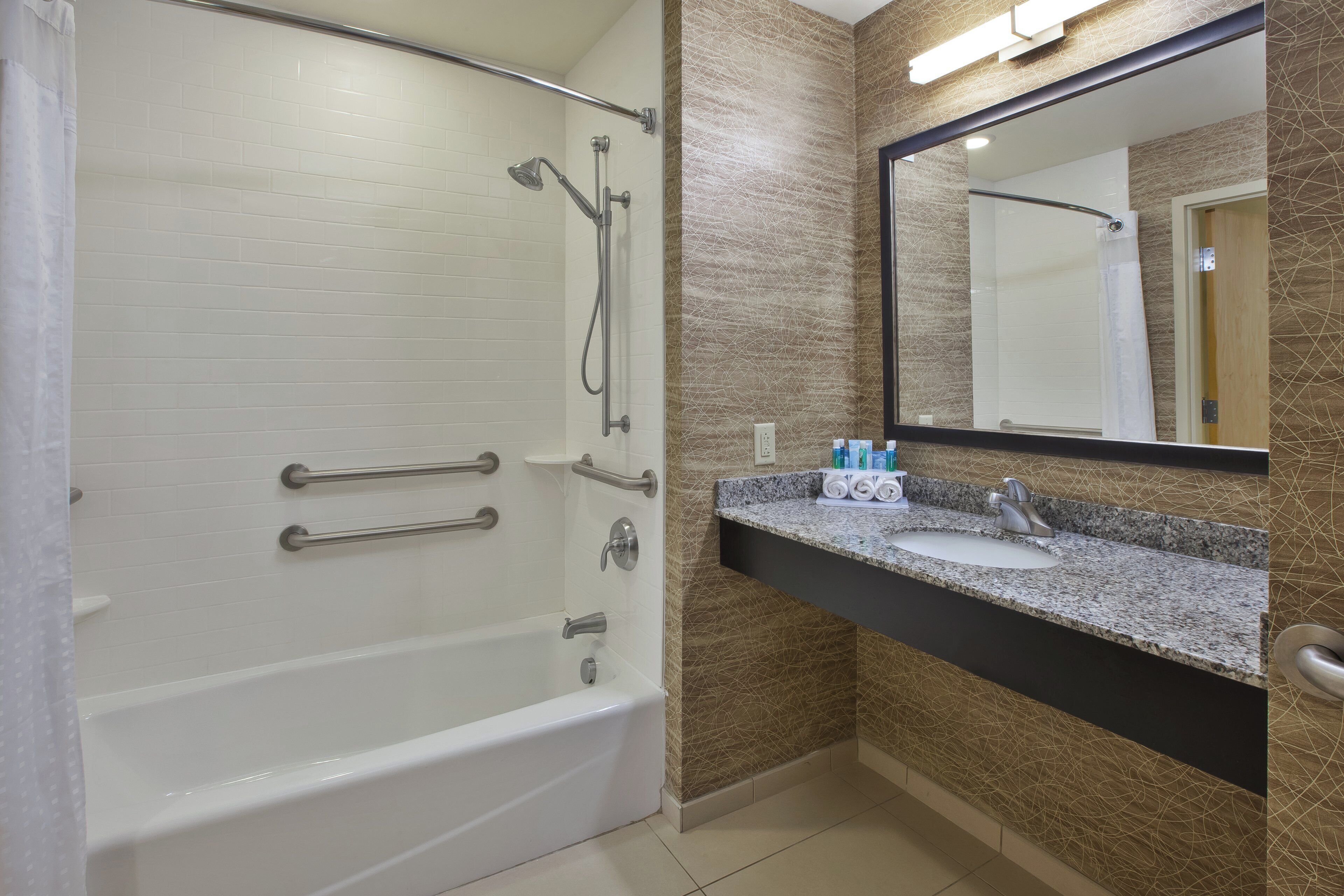 Un baño moderno con cabina de ducha, tocador de granito y un espejo grande.