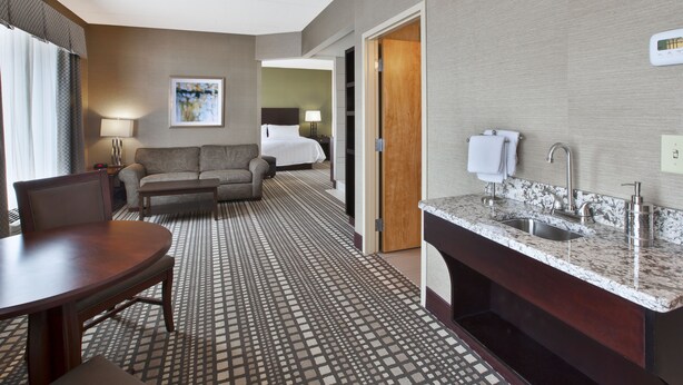 Une chambre d’hôtel comprenant une table à manger, un canapé, un lit, une salle de bain avec un lavabo et un miroir, et un sol à motifs.
