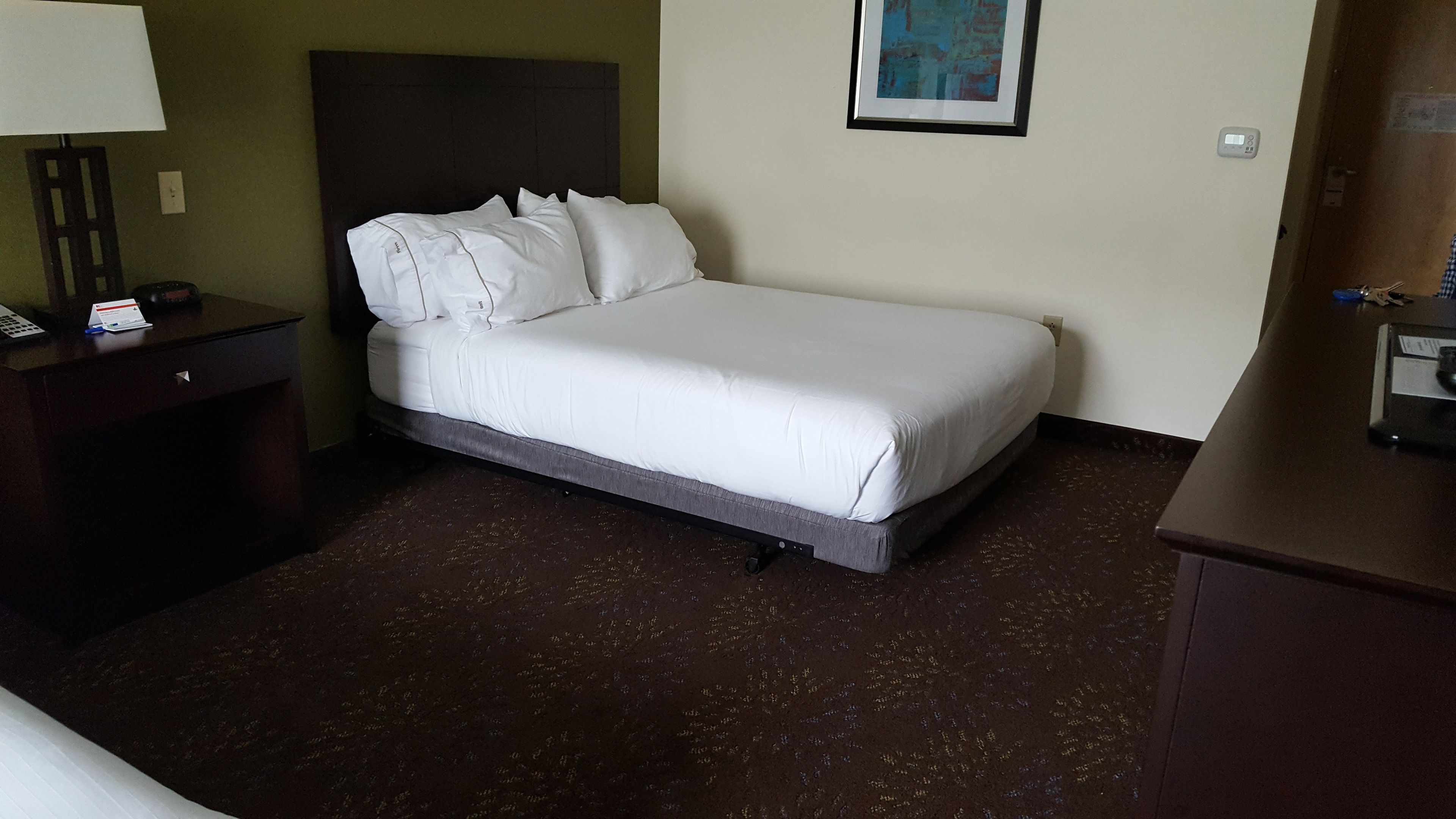 A hotel room with a single bed, a nightstand, a desk, and a wall-mounted light.