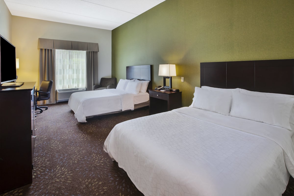 A hotel room with two beds, a desk with a chair, a TV, and a window with curtains.