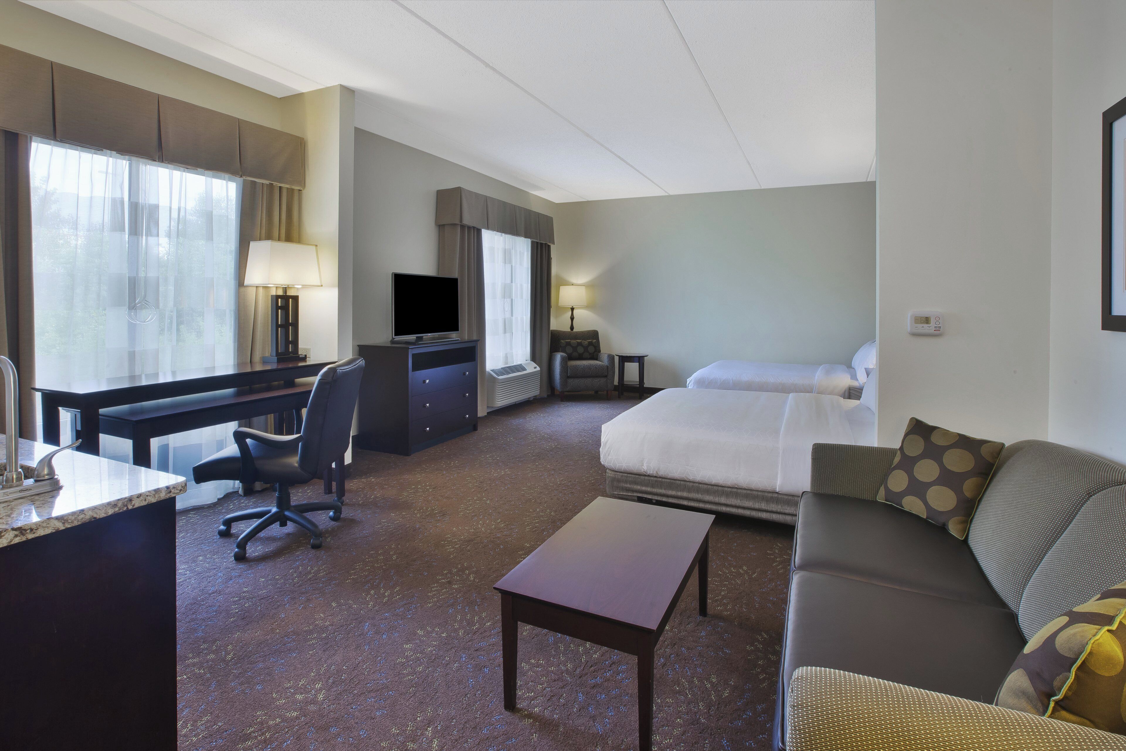 A hotel room with a bed, a desk, a chair, a sofa, and a television.