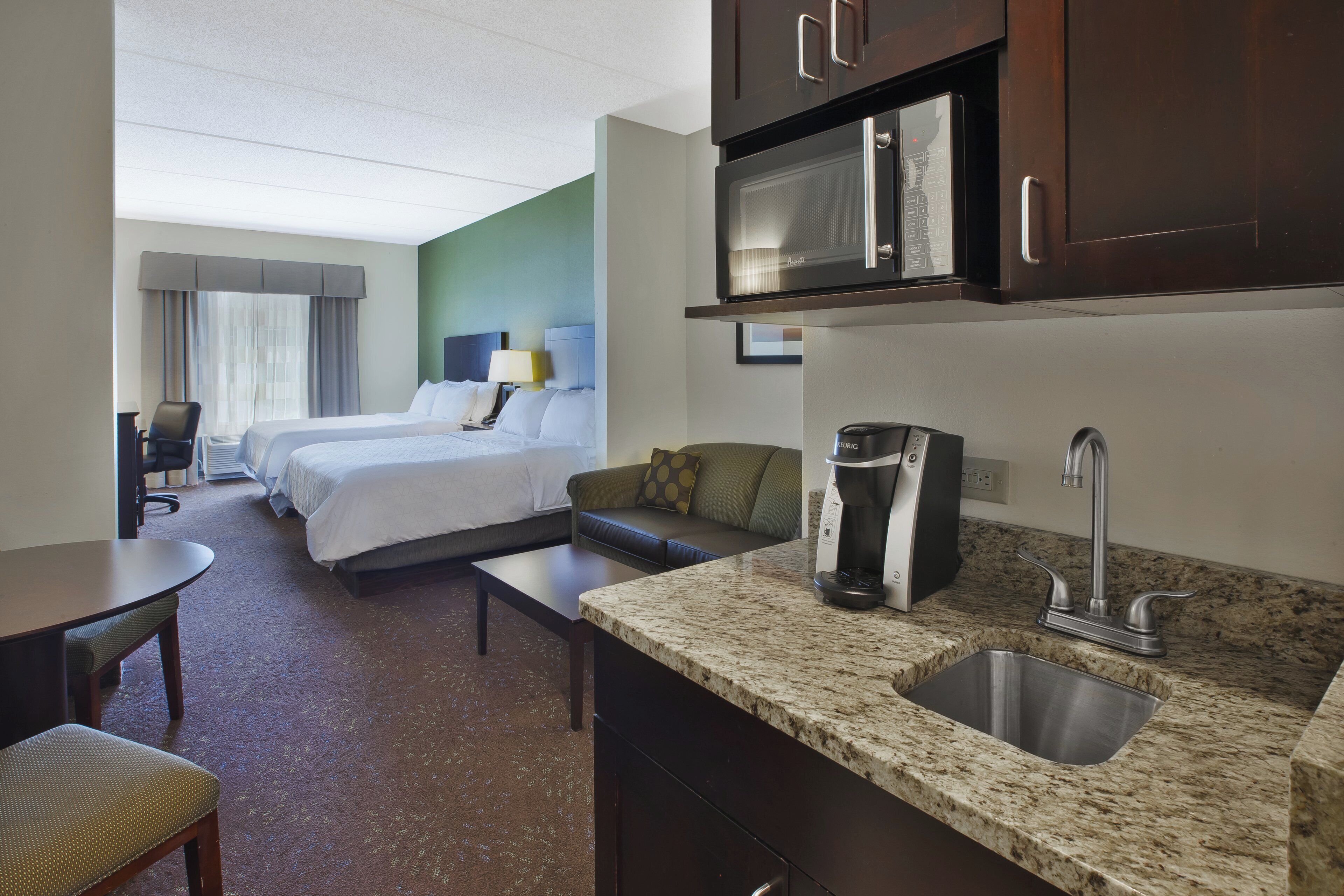 Quarto de hotel com cozinha compacta, cama, sofá e área de refeições.