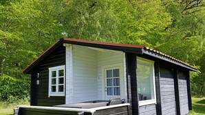 A small cabin with a single window and a door, surrounded by lush greenery. - Nordsjællands Feriepark & Camping (Alsgarde)