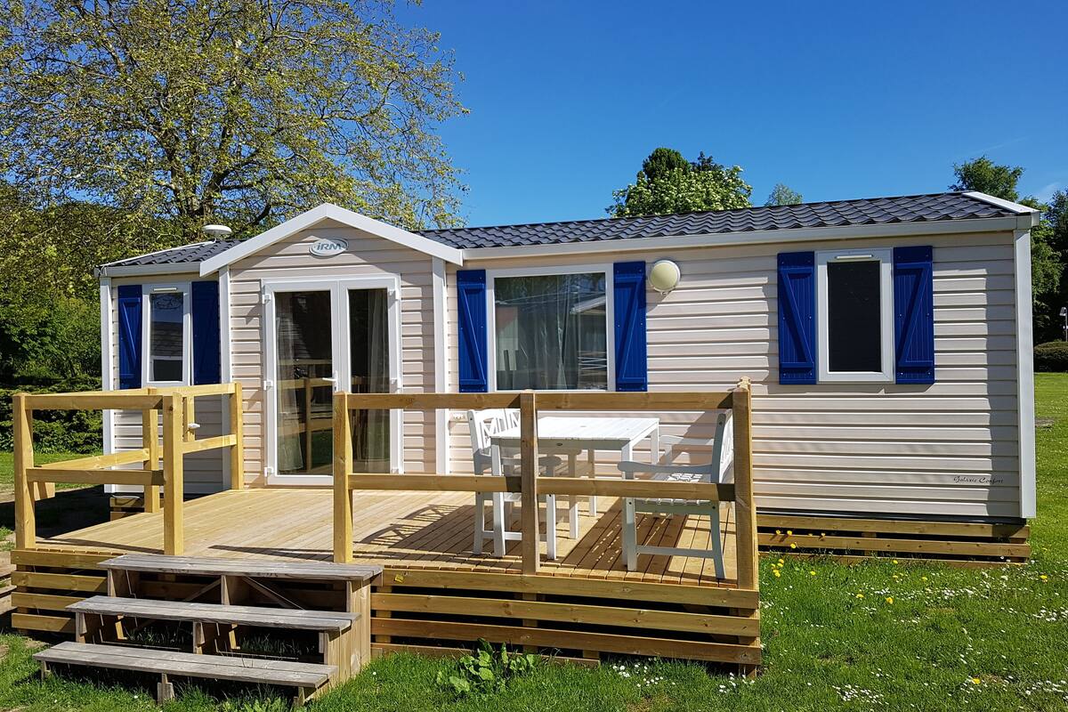 A mobile home with a deck and picnic tables.