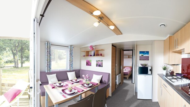 A modern RV interior with a dining area, kitchenette, and a view of the outdoors. - Nordsjællands Feriepark & Camping (Alsgarde)
