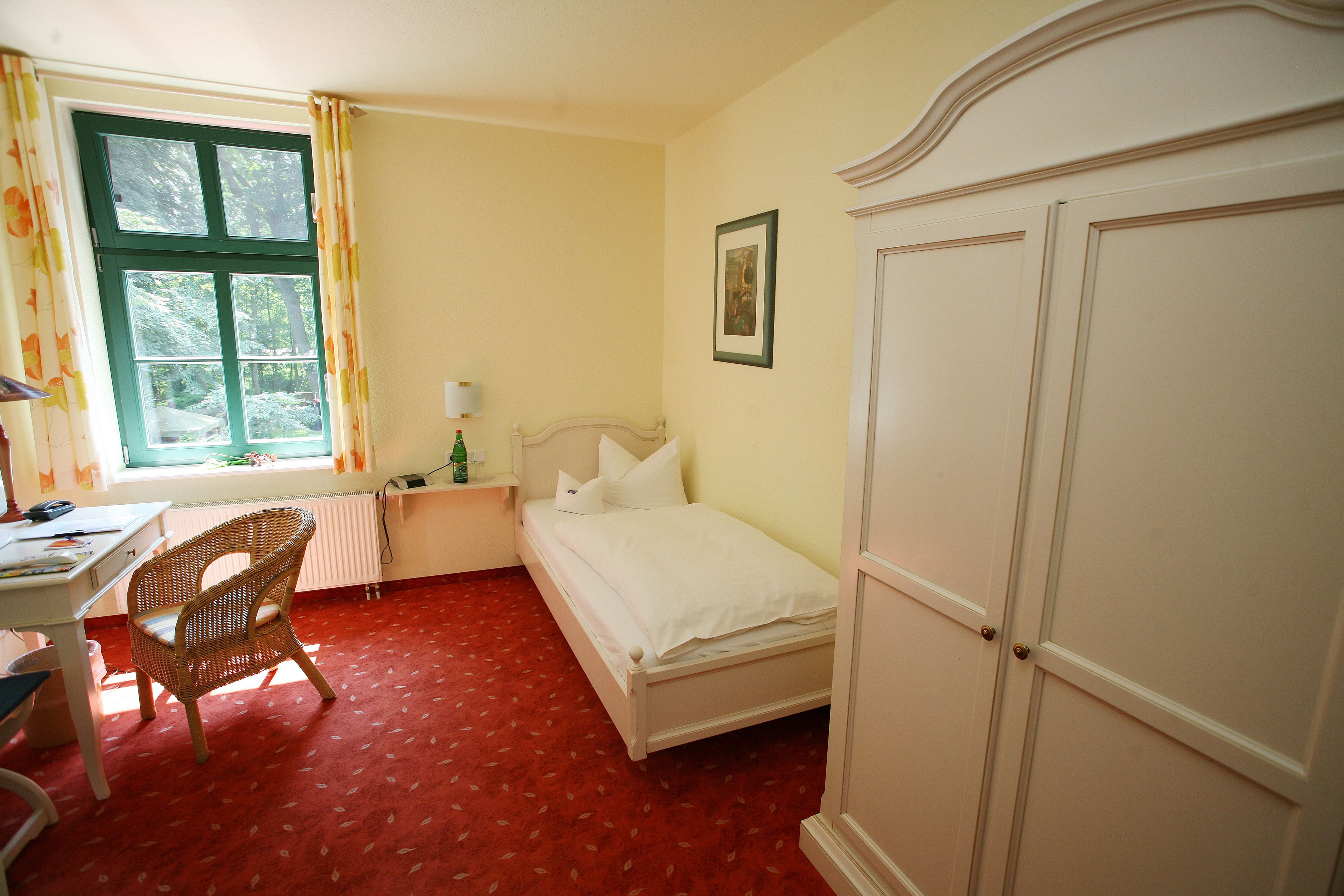 Een slaapkamer met een bed, een stoel, een bureau en een raam met gordijnen.