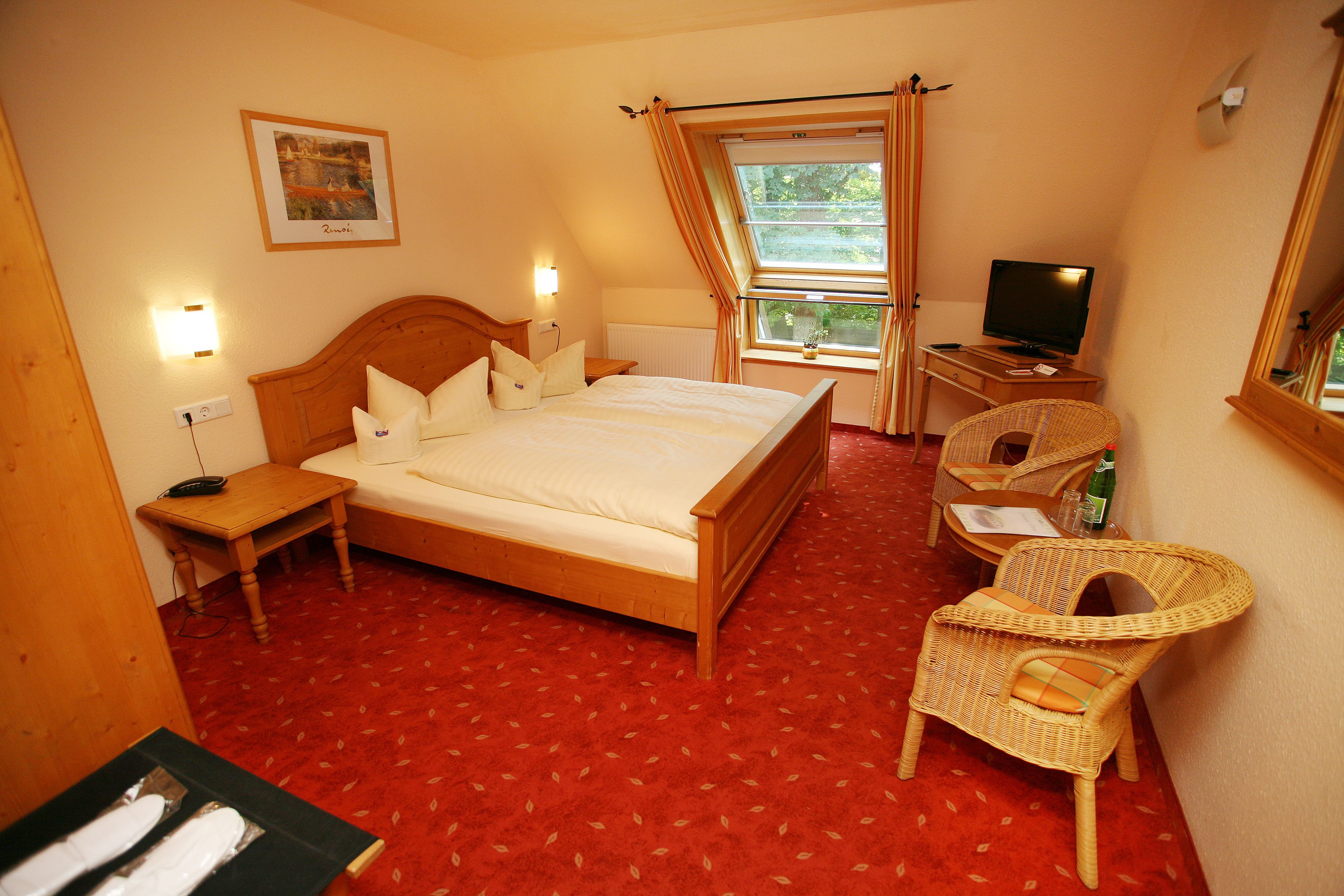 Une chambre d’hôtel avec un lit, une télévision, un fauteuil en osier et une fenêtre avec des rideaux.