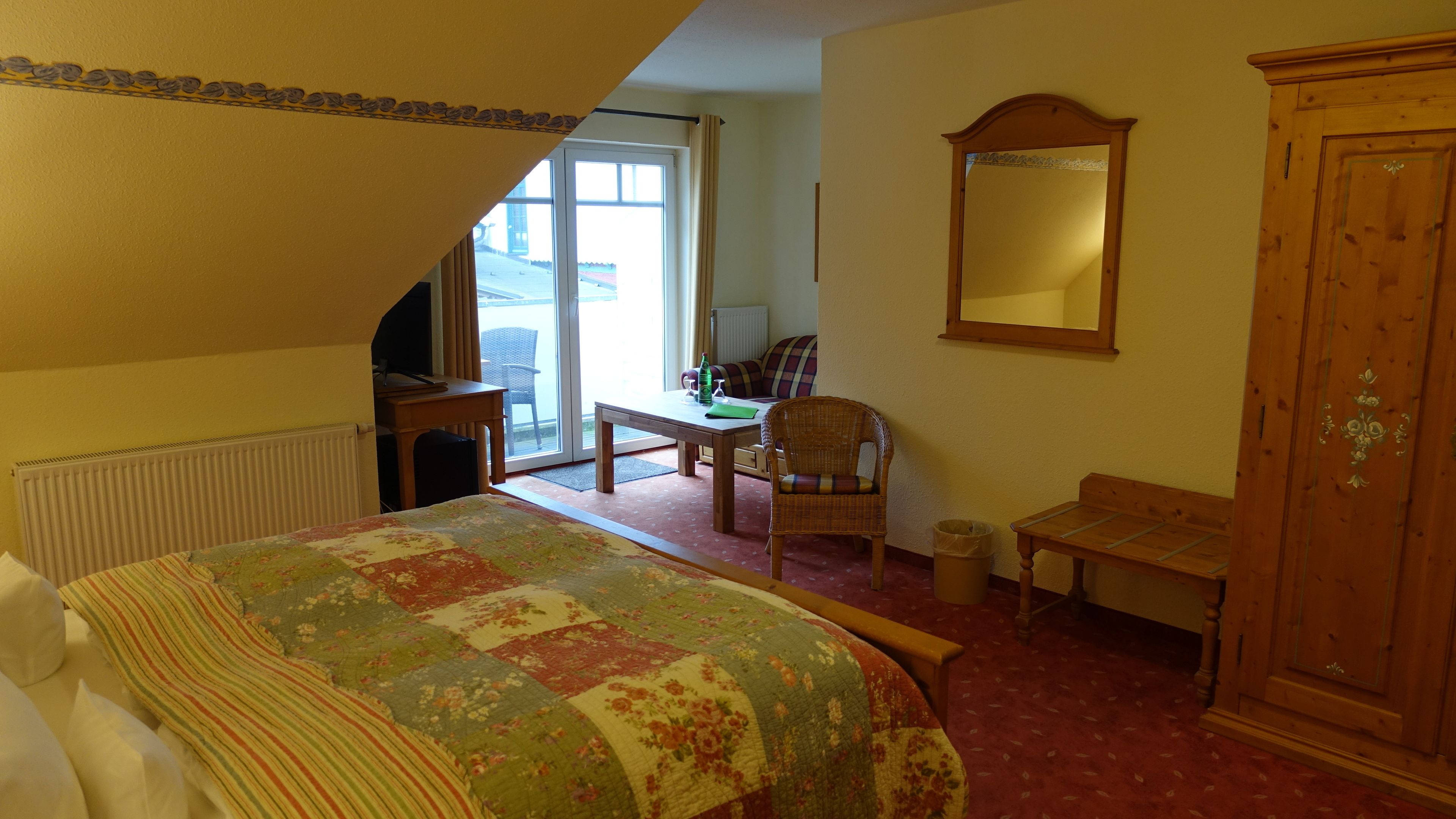 Une chambre d’hôtel avec un lit, une armoire en bois, une chaise, une table et une grande fenêtre.