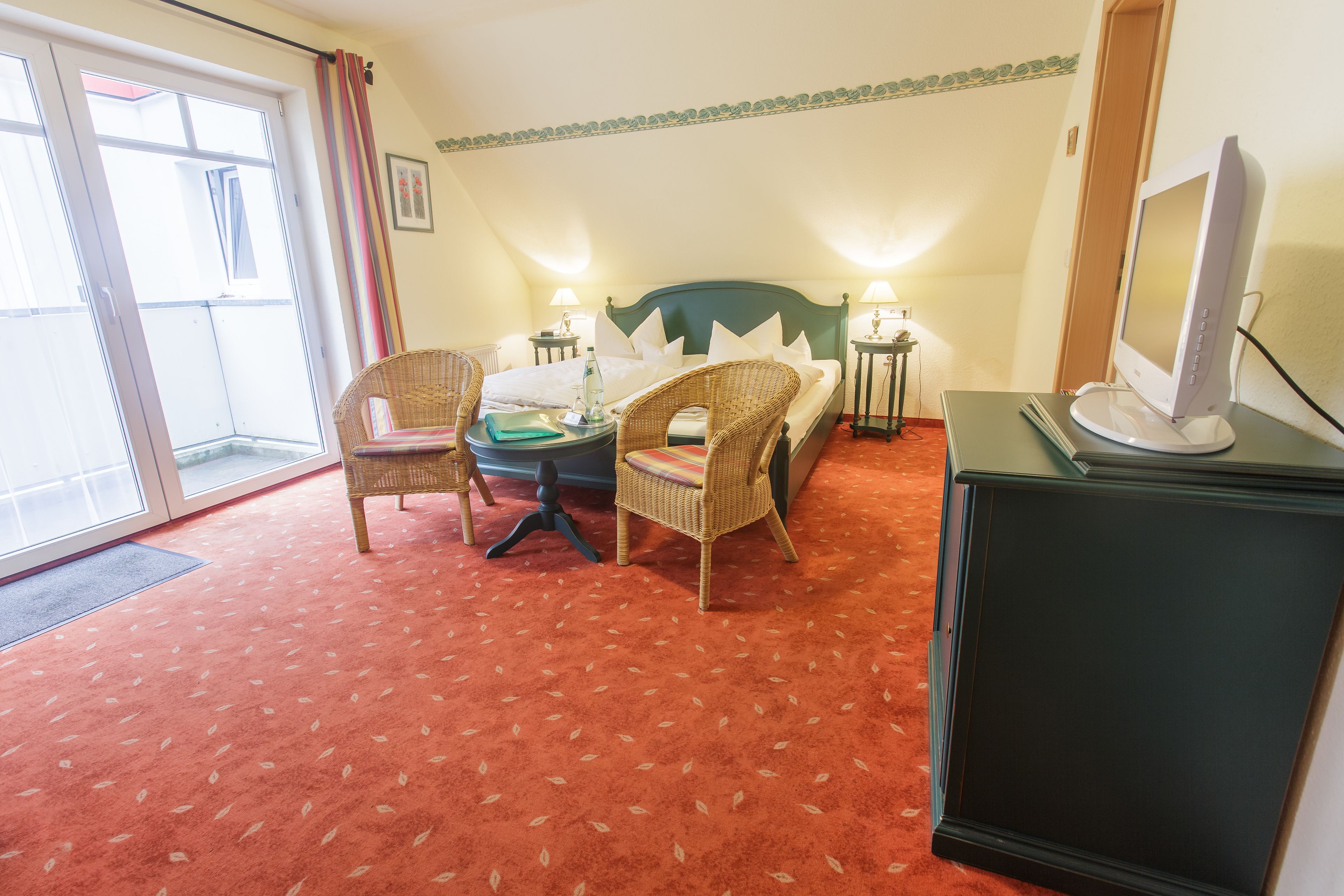 A hotel room with a bed, two chairs, a small table, a television, and a window with curtains.