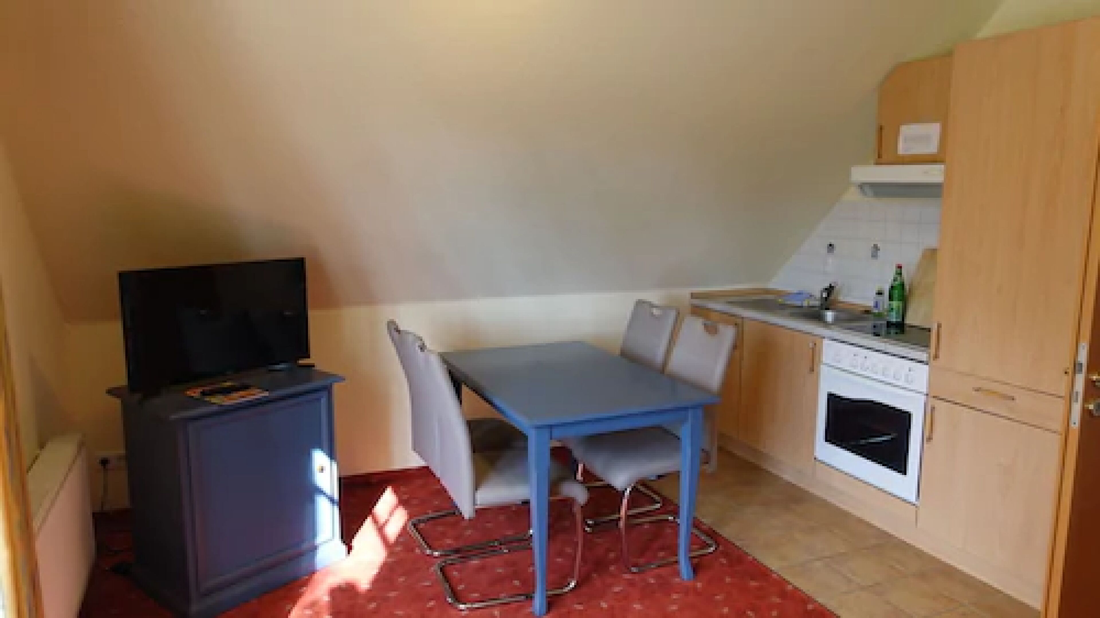 A compact kitchen with a dining table and chairs, a small cabinet with a television, and a white oven.