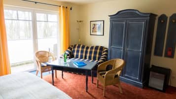 A room with a bed, a table with chairs, a sofa, a wardrobe, and a small table with a lamp.