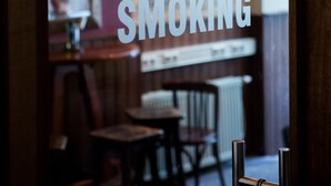 A restaurant interior with a visible 'SMOKING' sign, wooden furniture, and a brick wall. - The Flying Pig Uptown Hostel (Amsterdam)