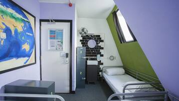 Een kleine, compacte kamer met twee eenpersoonsbedden, een bureau, een stoel, een wereldkaart aan de muur, een deur met een nummer en een klein raam.