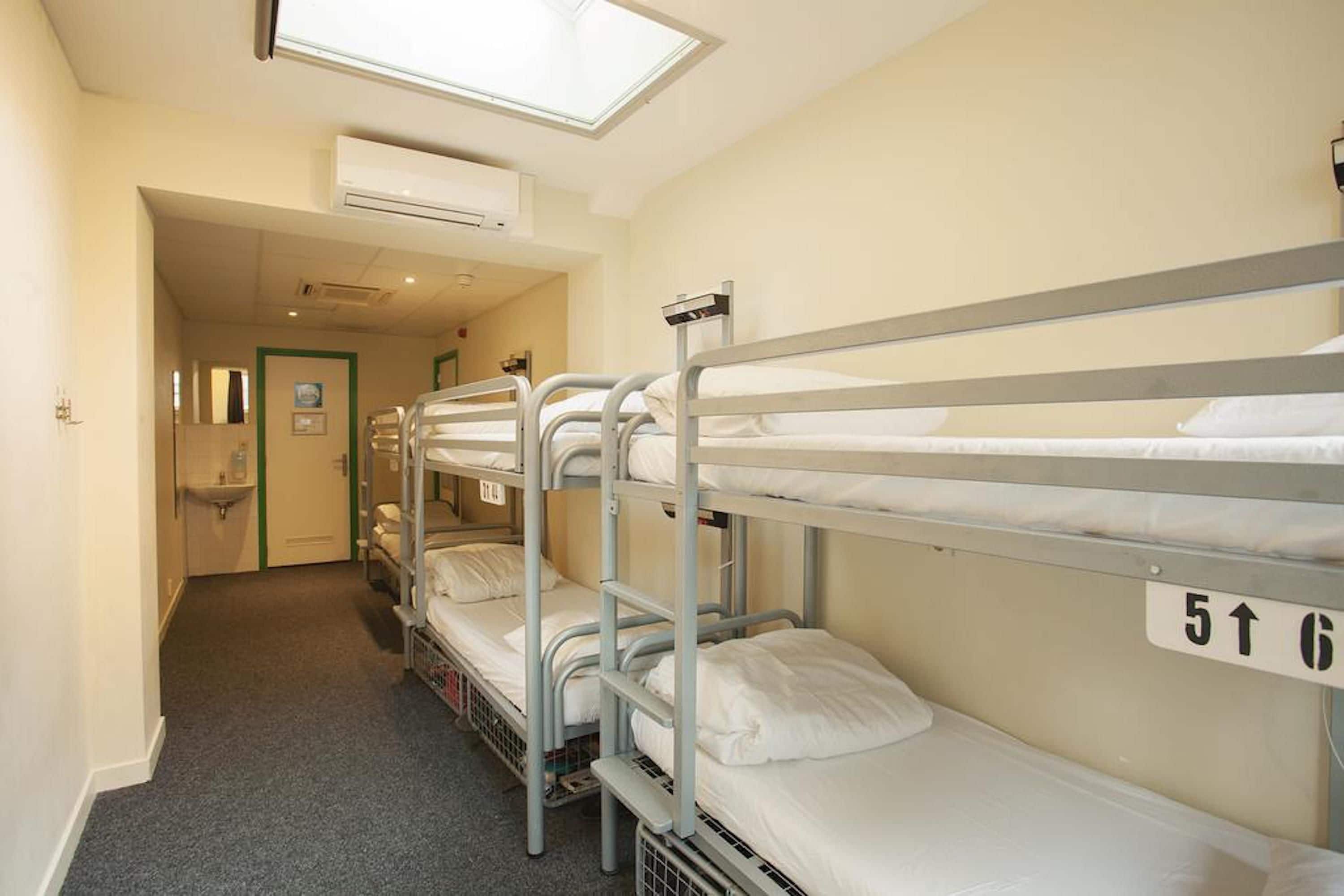 Une chambre de dortoir avec des lits superposés, un puits de lumière, un appareil de climatisation et une porte donnant accès à une salle de bain.