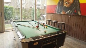 A pool table in a room with a large window, a mural on the wall, and a view of a garden. - The Flying Pig Uptown Hostel (Amsterdam)