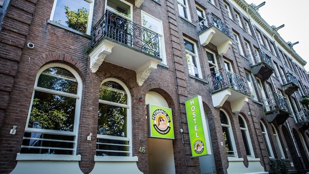 A brick building with multiple windows and balconies. There are two green signs on the building, one with a logo and the text "FlyingPig Inn" and another with the text "HOSTEL". - The Flying Pig Uptown Hostel (Amsterdam)