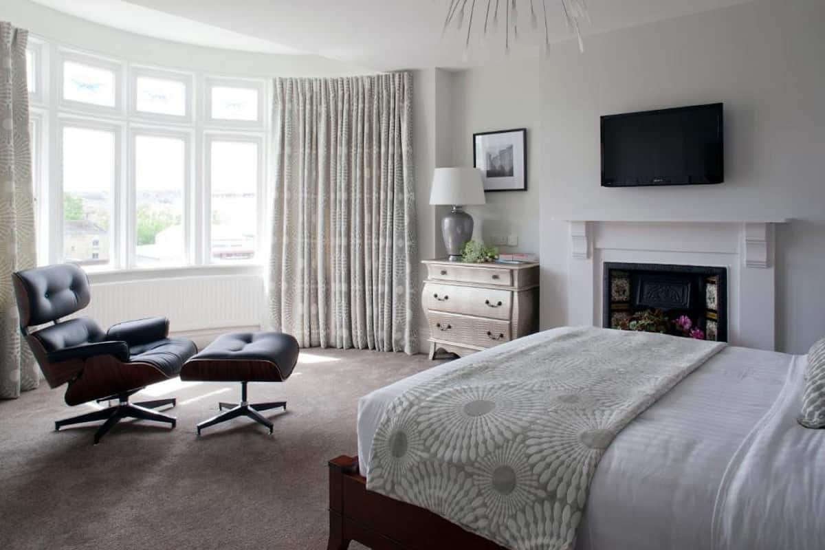 A bedroom with a large bed, a chair, a dresser, a TV, and a fireplace.