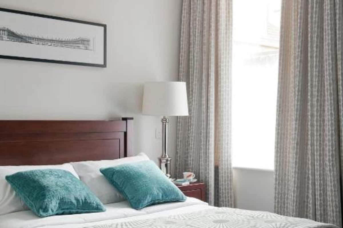 A neatly made bed with a patterned bedspread, a bedside lamp, and curtains on a window.