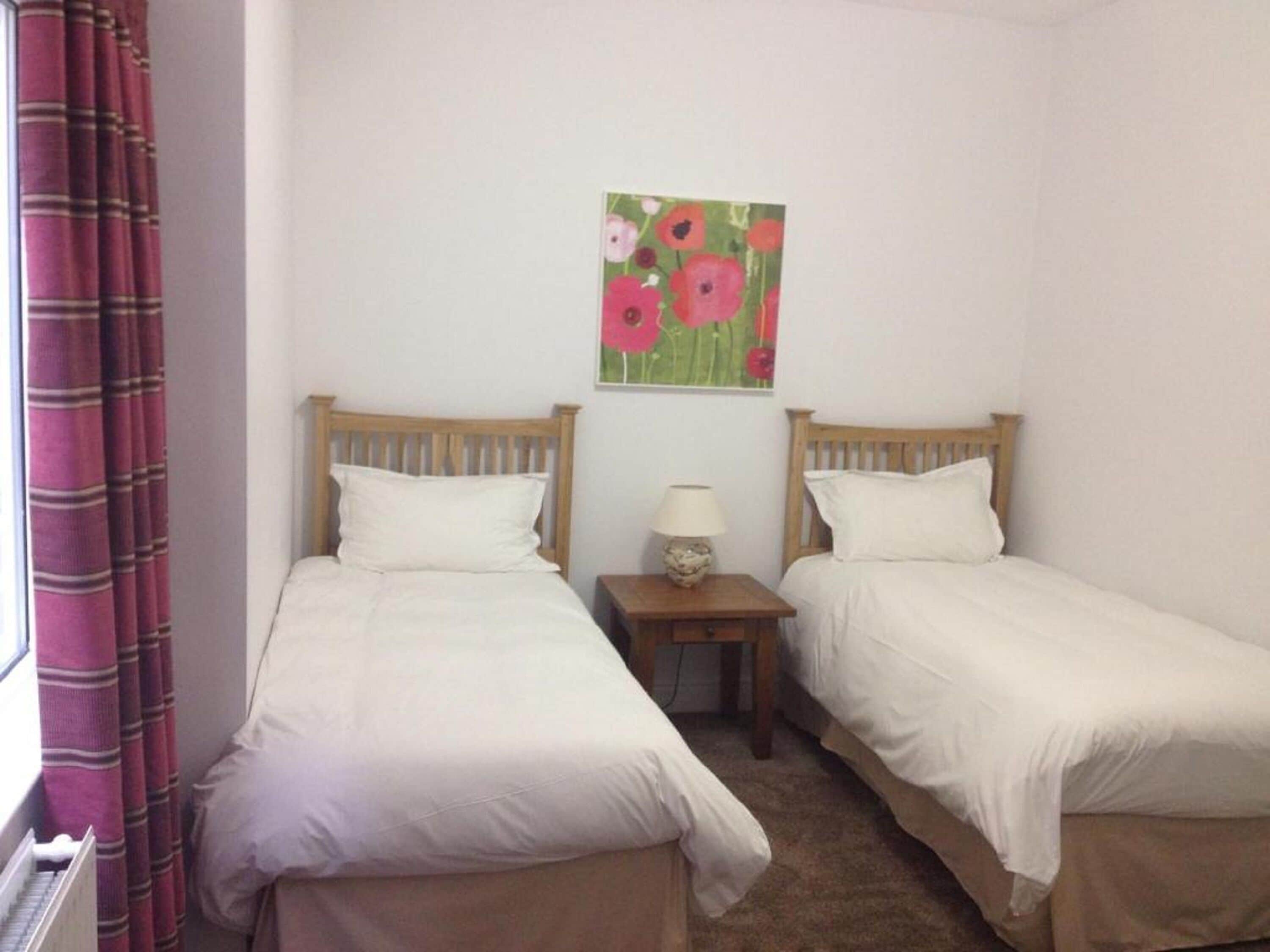 Una habitación con dos camas individuales, una mesita de noche con lámpara y un cuadro de flores en la pared.