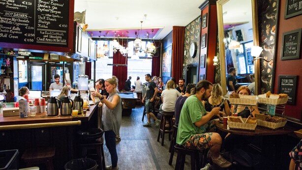 Un bar animé, avec un tableau affichant le menu, des tabourets et un miroir qui reflète l’intérieur.