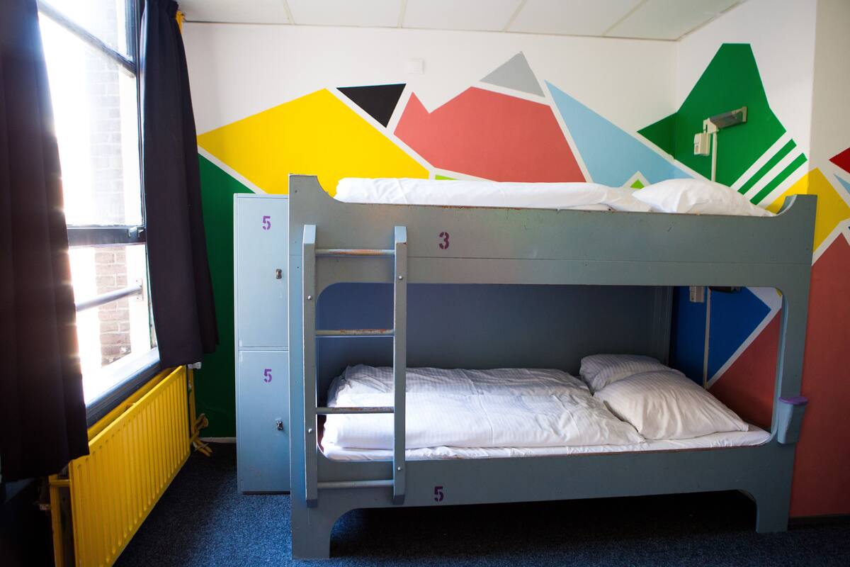 Een stapelbed met een ladder, een radiator en een raam met gordijnen.