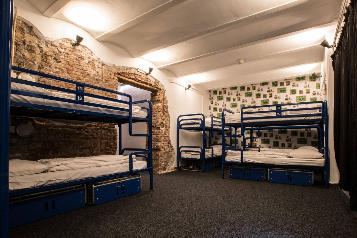 Een studentenkamer met stapelbedden, genummerd van 9 tot 12, en een stenen muur.