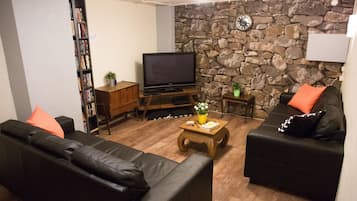 Ein Wohnzimmer mit einer Steinsäule, einem Fernseher, einem Bücherregal und zwei schwarzen Sofas mit orangefarbenen Kissen.