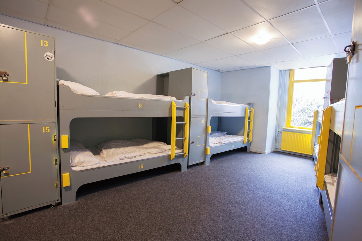 Een slaapzaal met stapelbedden, kasten en een raam met uitzicht.