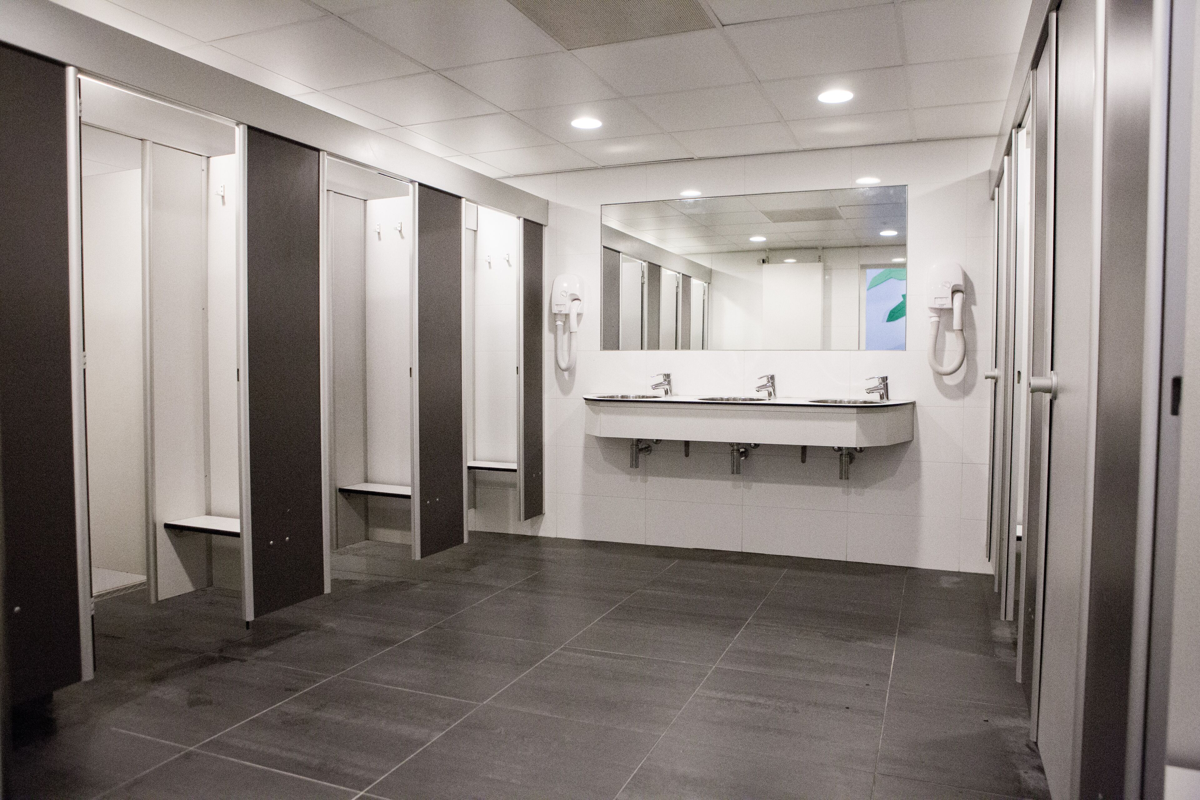 A modern restroom with multiple stalls, a large mirror, and a central sink area.