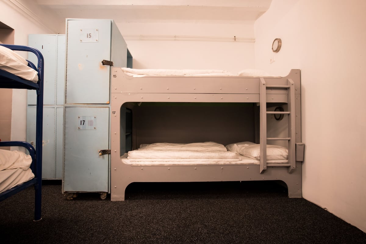 Een slaapkamer met een stapelbed, een blauwe metalen garderobe en een klein kastje.
