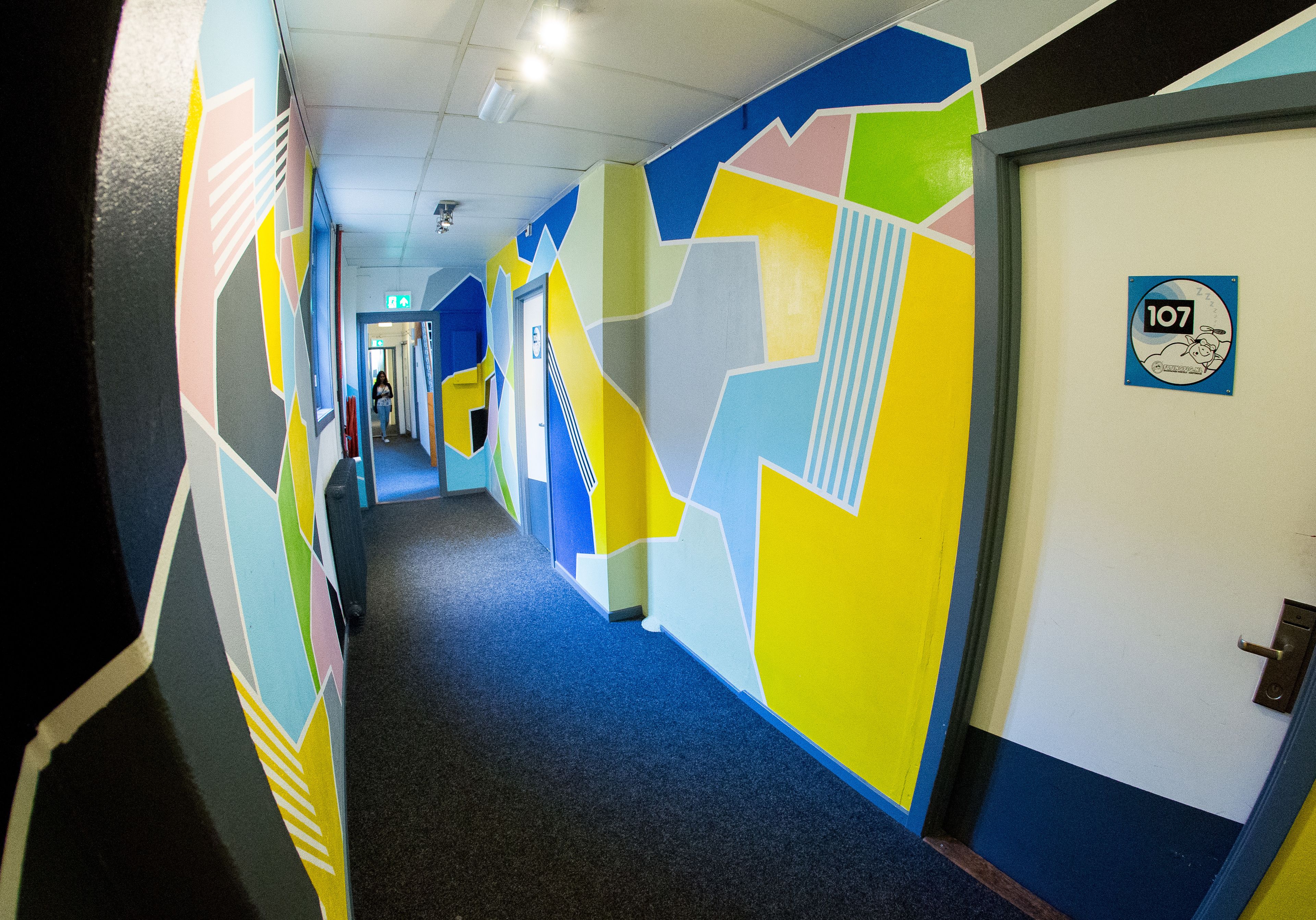 A hallway with colorful geometric wall designs and a door marked with the number 107.