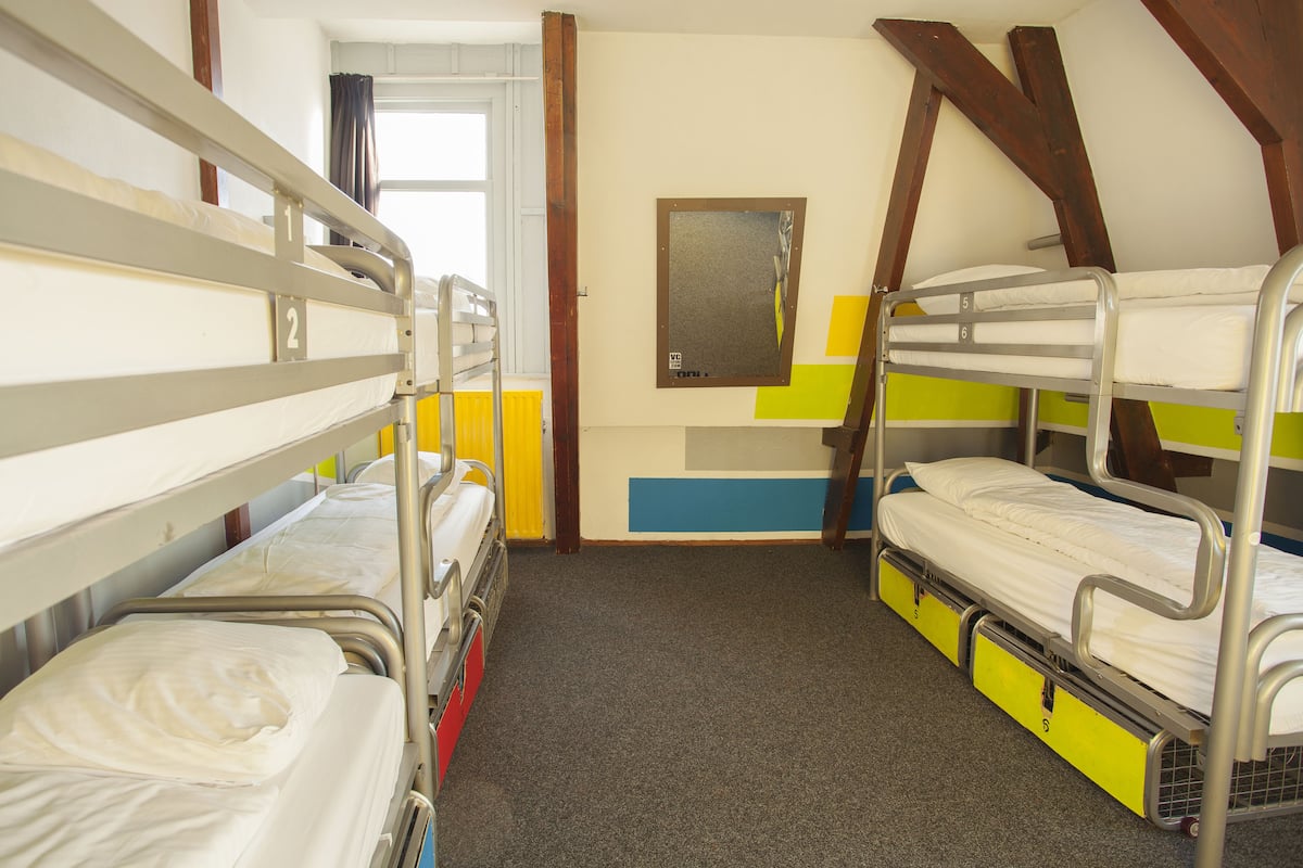 Een kamer met stapelbedden, een raam met gordijnen, een spiegel aan de muur en een deur.