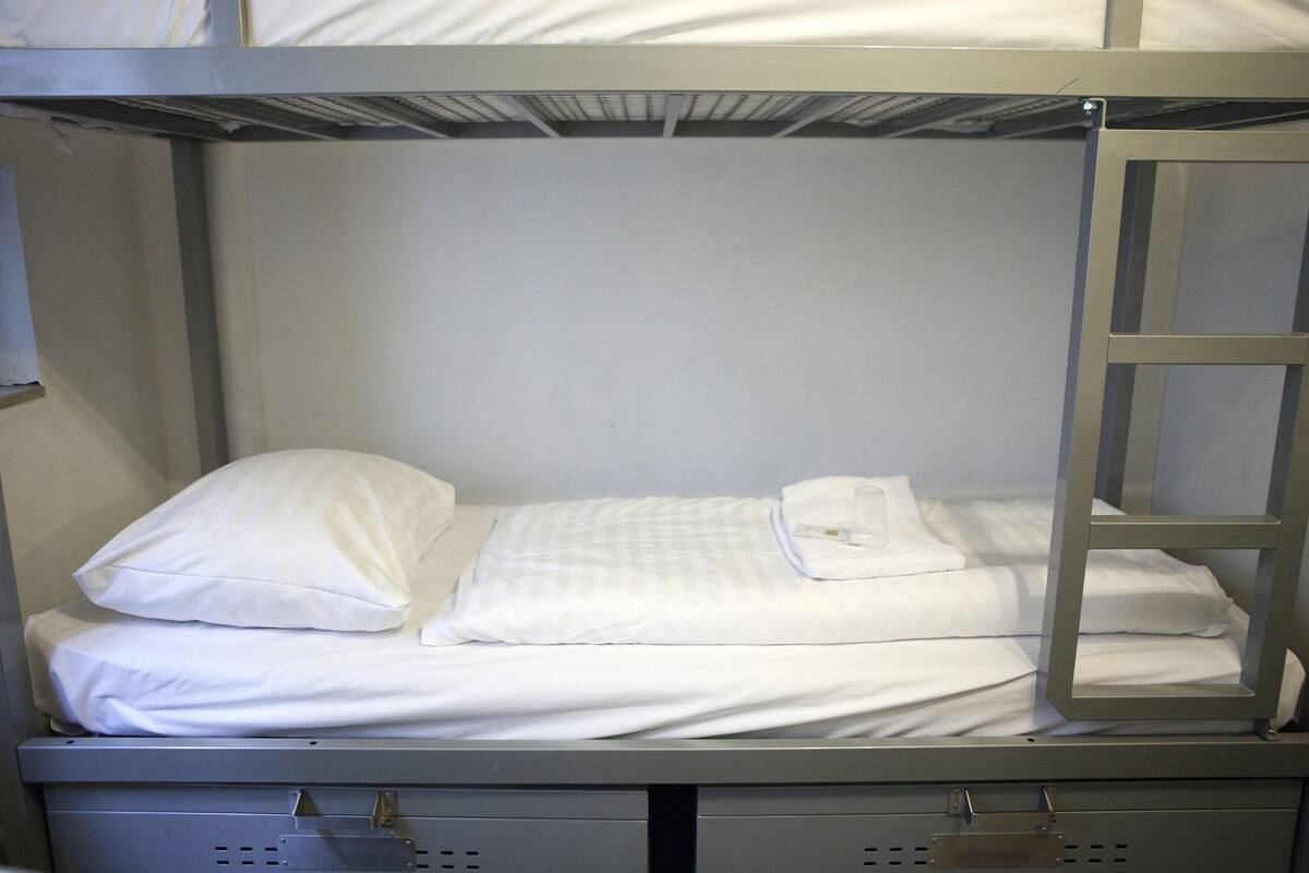 Een stapelbed met witte beddengoed en een metalen ladder.