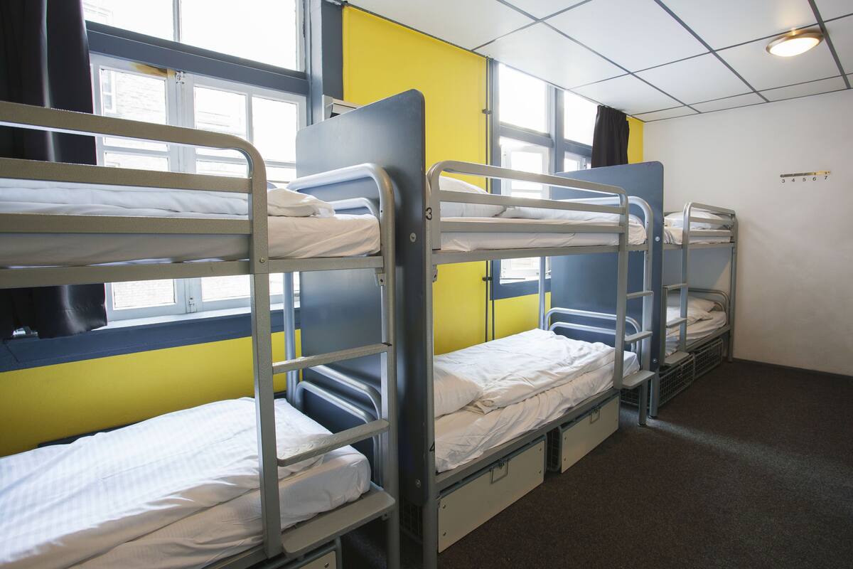 Een slaapzaal met drie stapelbedden, elk met een matras en een kussen.