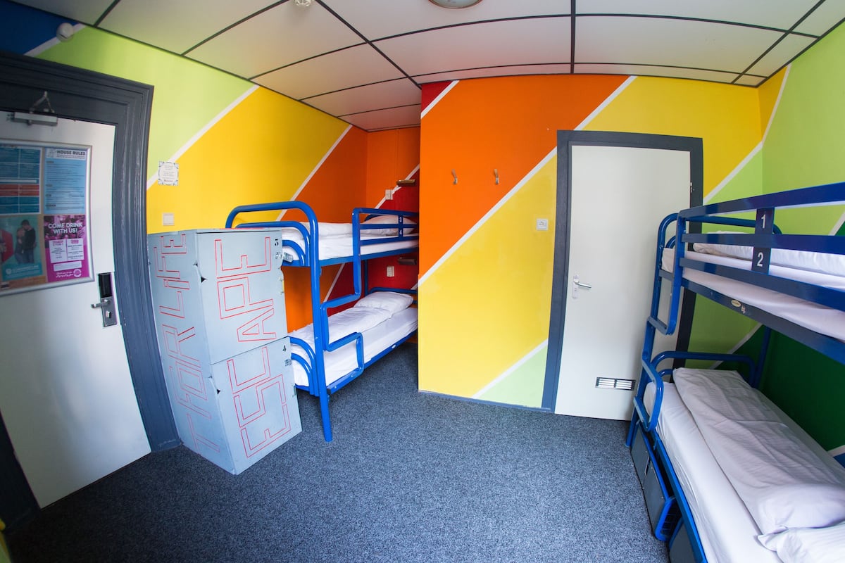 Een slaapzaal met stapelbedden, een deur en een muur met geometrische patronen.