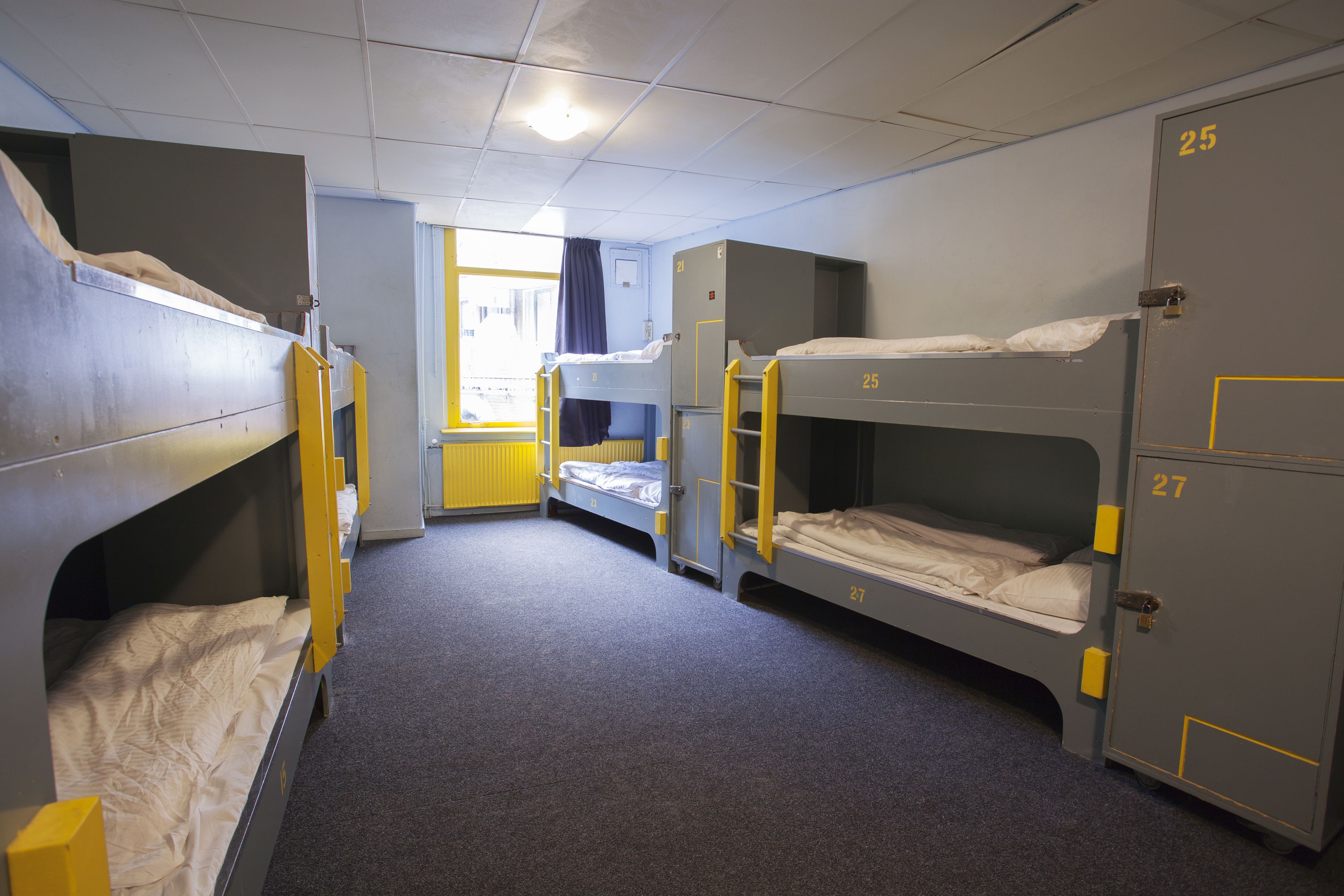 Ein Schlafsaalzimmer mit Stockbetten, einem Fenster mit Vorhängen und Ablusfachränken.