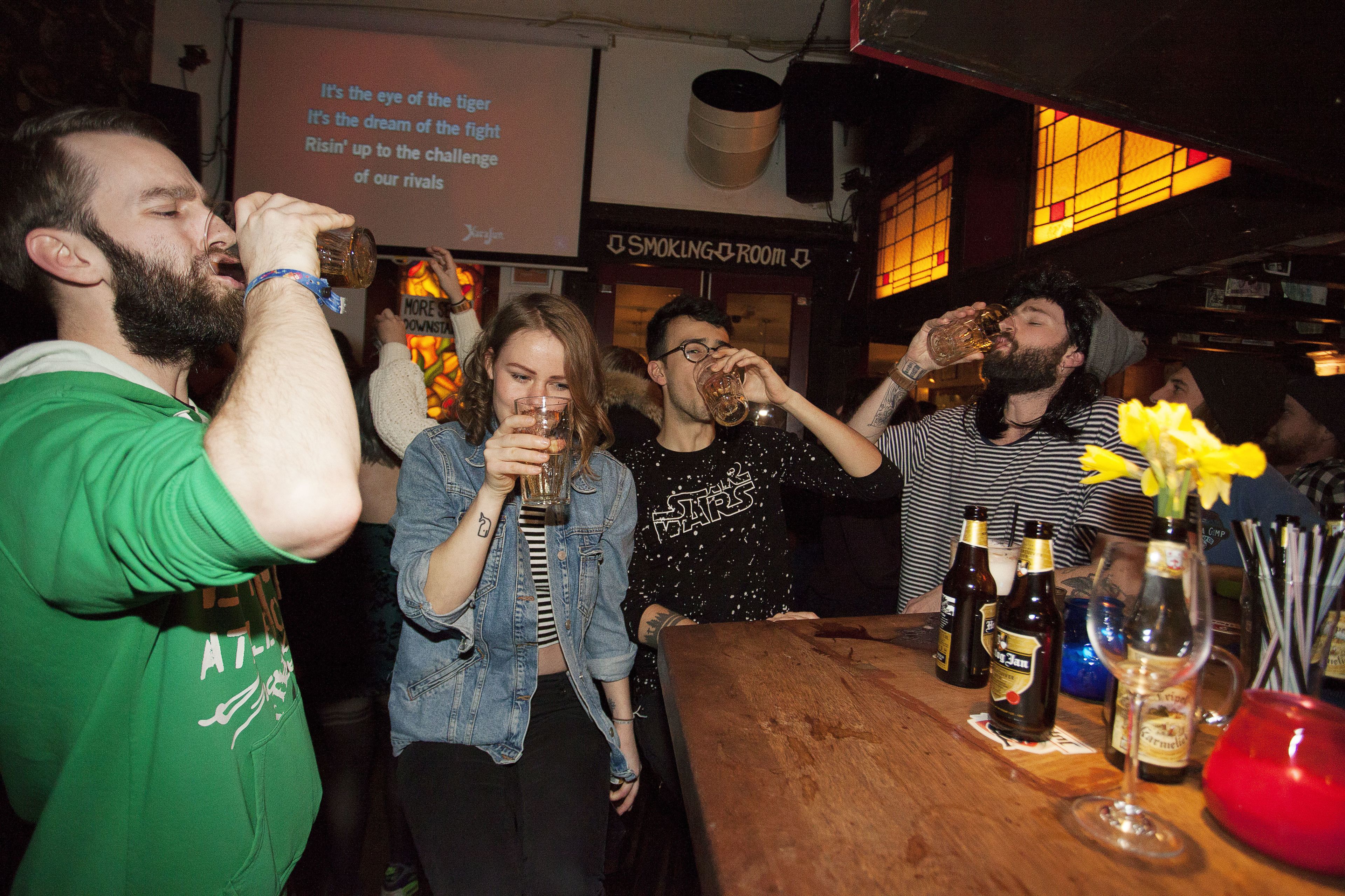 Un grupo de personas en un bar con una mesa de madera, botellas y vasos.