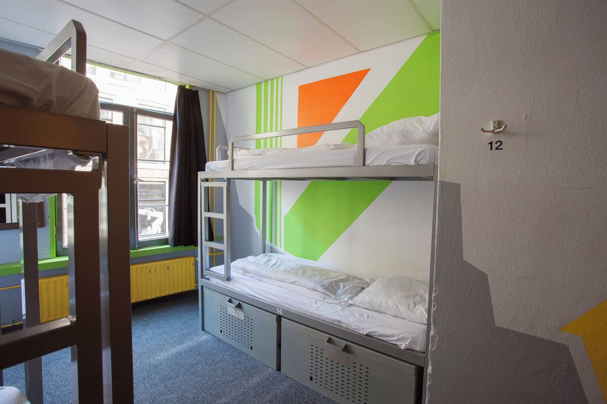 Een slaapkamer met een stapelbed, een raam, een deur met het nummer 12 en een radiator.