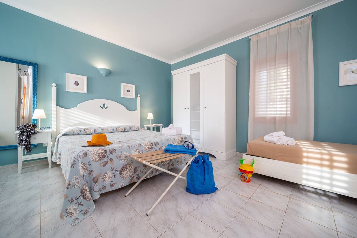 A bedroom with a bed, a wardrobe, a bedside table, and a window with curtains.