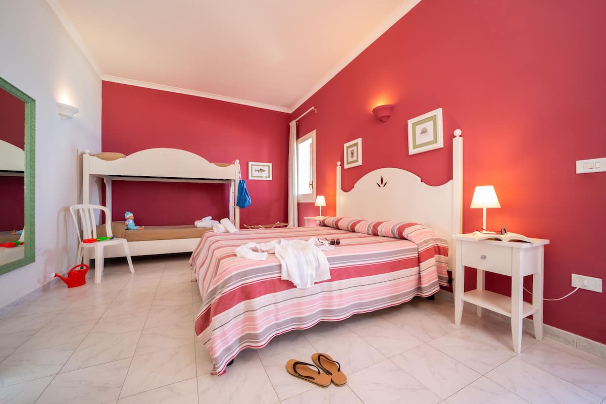 A bedroom with a bunk bed, a bedside table with a lamp, a chair, and a red wall.