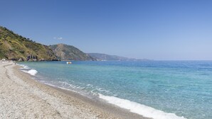 A pebble beach with clear blue water and a hilly backdrop. - TH Gioiosa Marea - Capo Calavà Village (Gioiosa Marea)