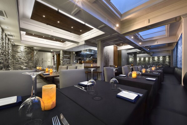 Un restaurante moderno con manteles negros, mesas iluminadas con velas y un fondo de pared de piedra.